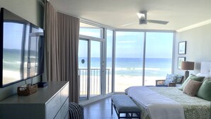 Un dormitorio con cama, un banco, un televisor y vista a la playa.