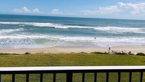 Una playa con olas, una zona cubierta de césped y una persona caminando.