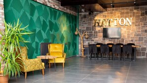 A lobby with a green patterned wall, a yellow armchair, a black sofa, a wooden side table, and a row of black chairs. - Hatton Suites Esenboga (Ankara)