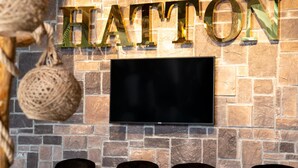 A stone wall with the word "HATTON" in gold letters and a flat-screen TV mounted above it. - Hatton Suites Esenboga (Ankara)
