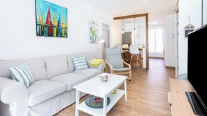 Un soggiorno moderno con un divano, un tavolino da caffè e una televisione. Al muro è appeso un quadro e sullo sfondo si nota un'area pranzo.
