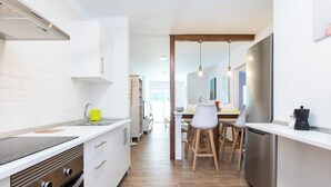 Una cucina moderna con mobili bianchi, piano cottura integrato e zona pranzo in legno con sedie.