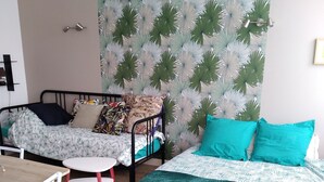 Une pièce comprenant un lit, une chaise, une petite table et un mur orné d’un motif de feuilles.