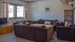 Ein Wohnzimmer mit braunen Sofas, einem Couchtisch, einem Fernseher auf einer Holzkommode und einem Bild an der Wand.