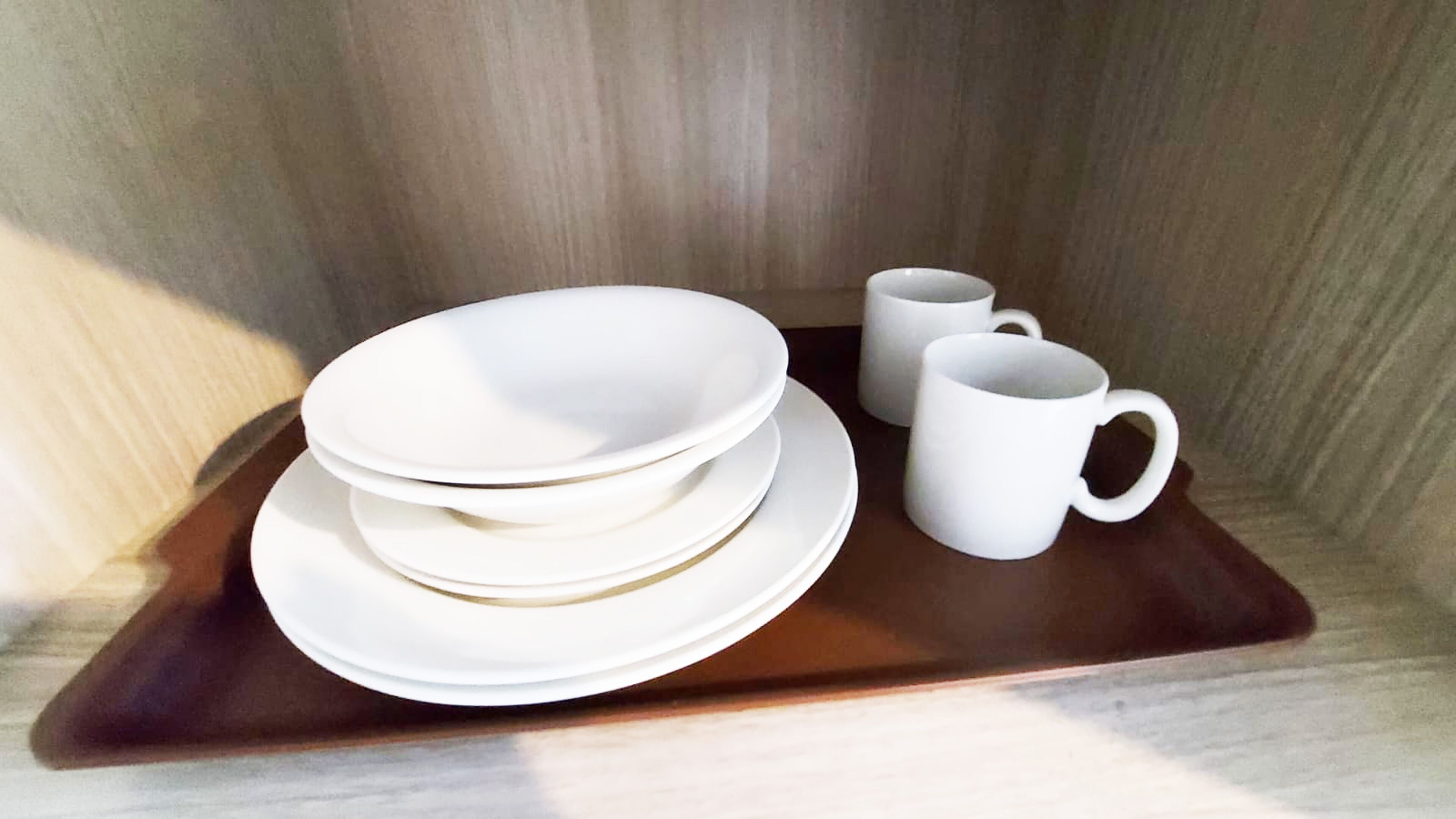 Un juego de platos y tazas blancas sobre una bandeja de madera.