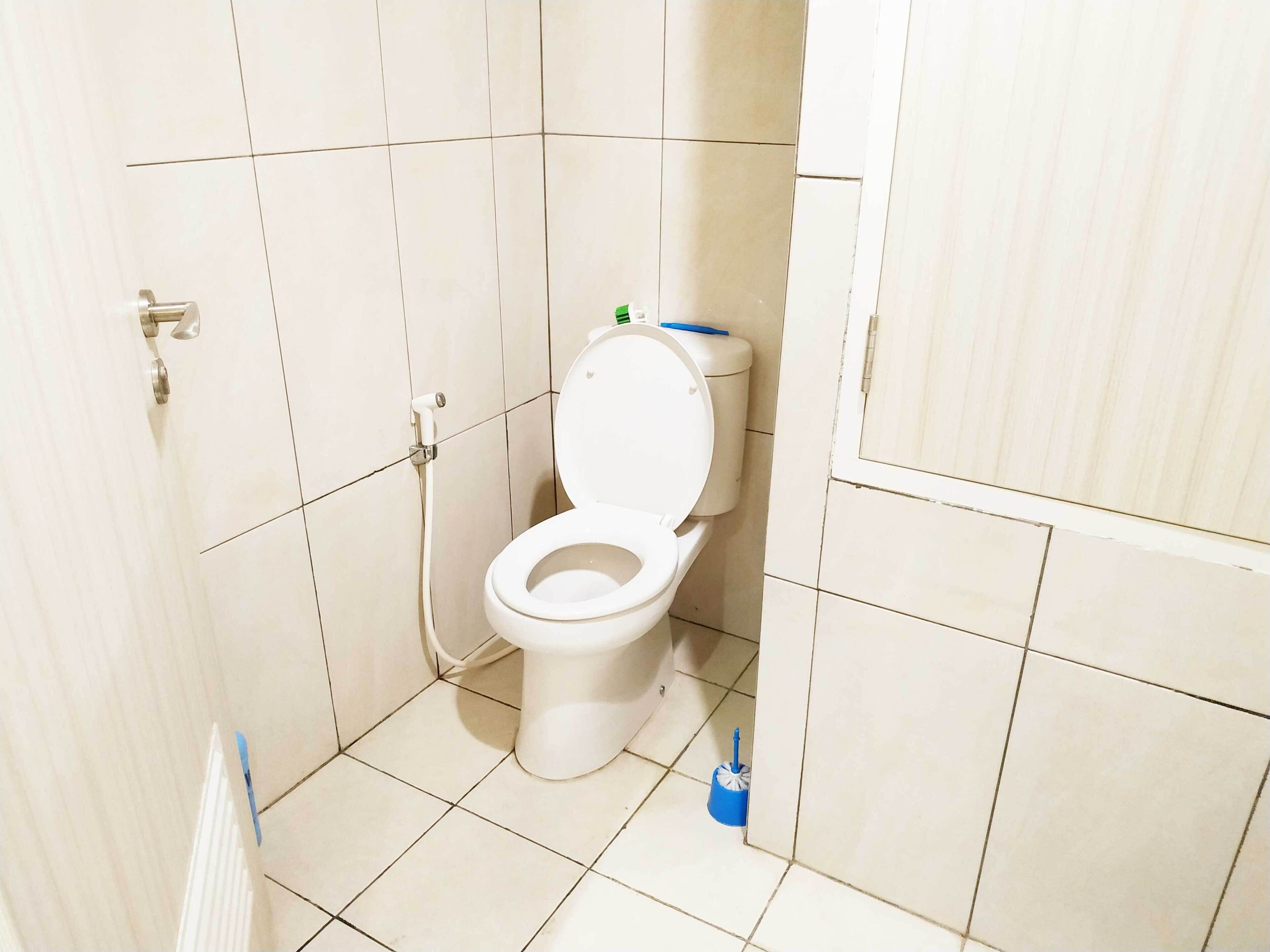 A small, clean bathroom with a toilet, a hand dryer, and a blue cleaning brush on the floor.