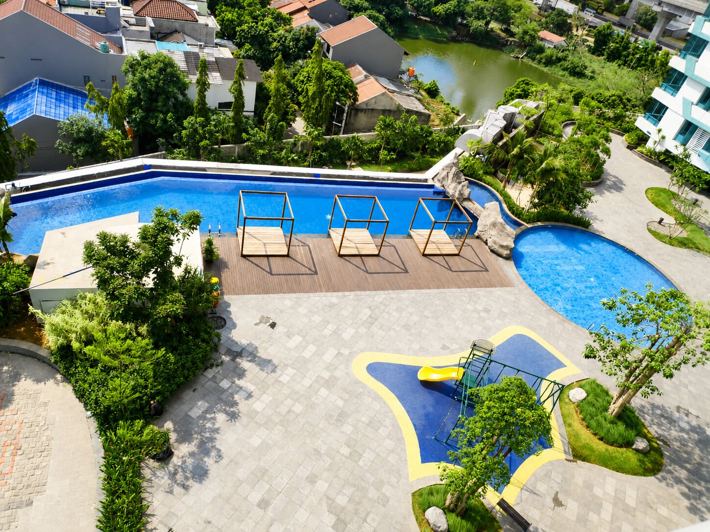 Piscina con tobogán, rodeada de vegetación y una zona pavimentada con sillas de descanso.