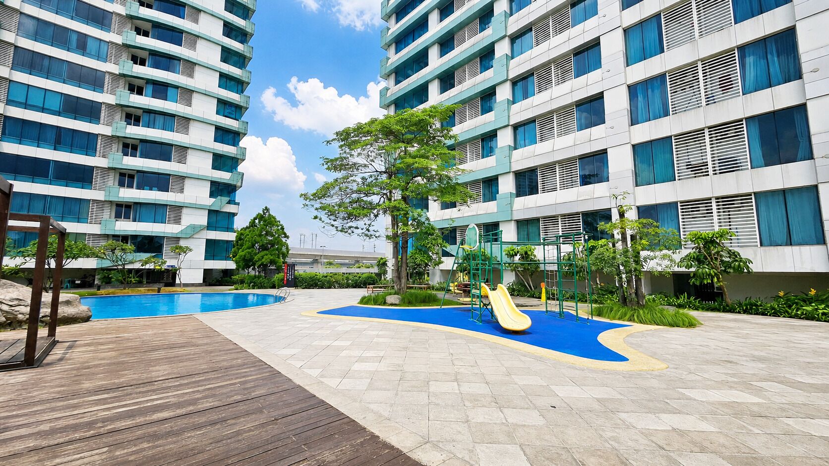 A residential building with a swimming pool, playground, and a wooden deck.