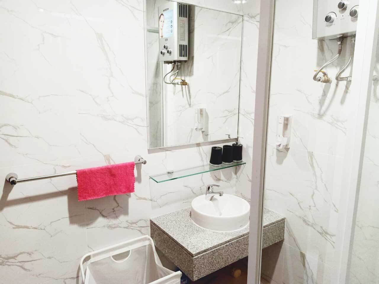 A bathroom with a marble wall, a glass shower enclosure, a white sink, and a pink towel.