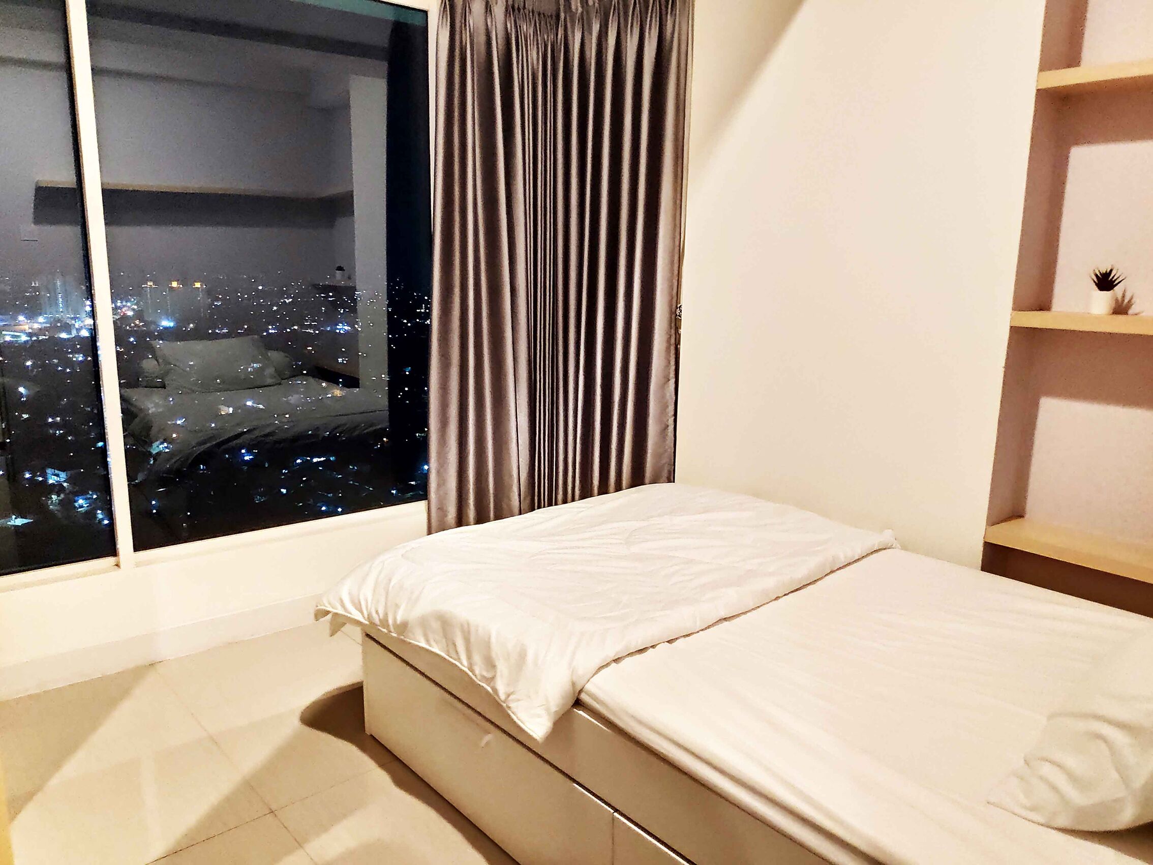 A bedroom with a large window, a bed, a curtain, and a shelf.