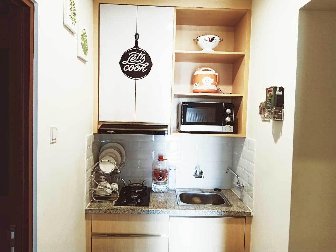 A compact kitchen with a microwave, stove, sink, and a 'Let's Cook' sign.
