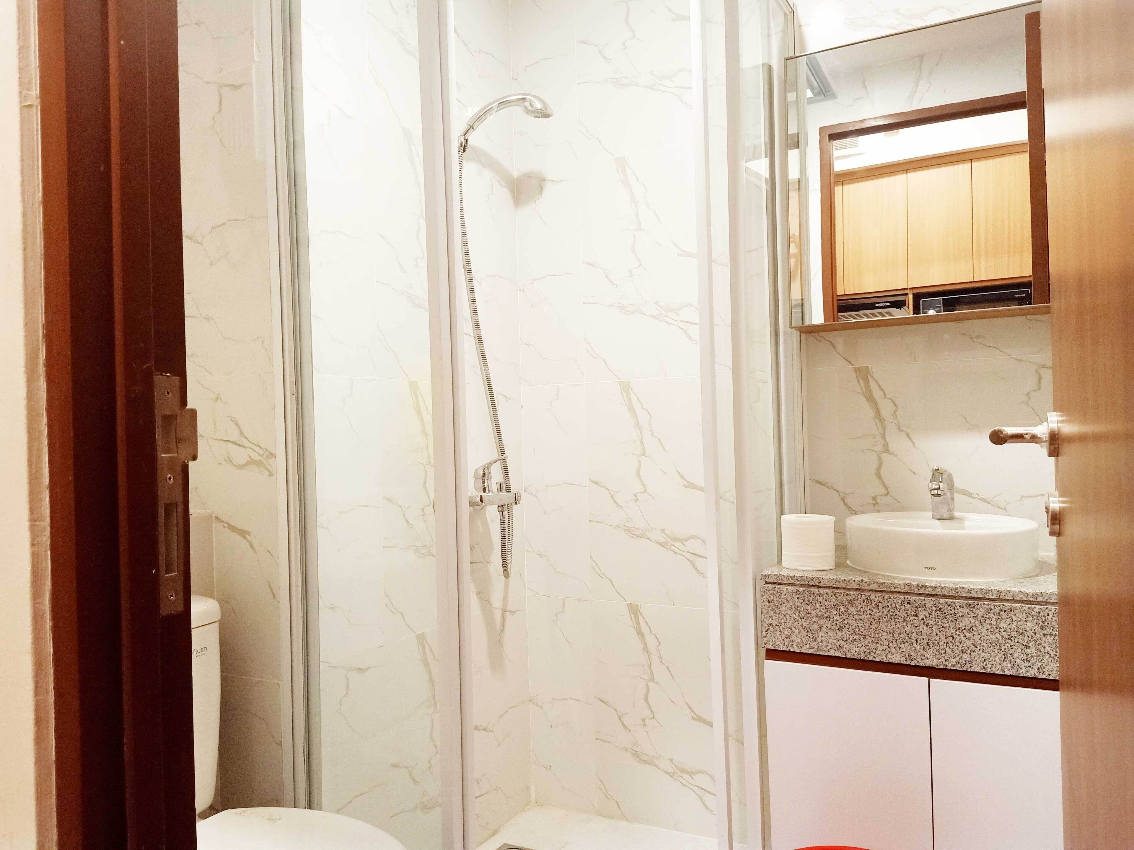 A bathroom with a glass-enclosed shower, a toilet, a sink with a mirror above it, and wooden cabinets.
