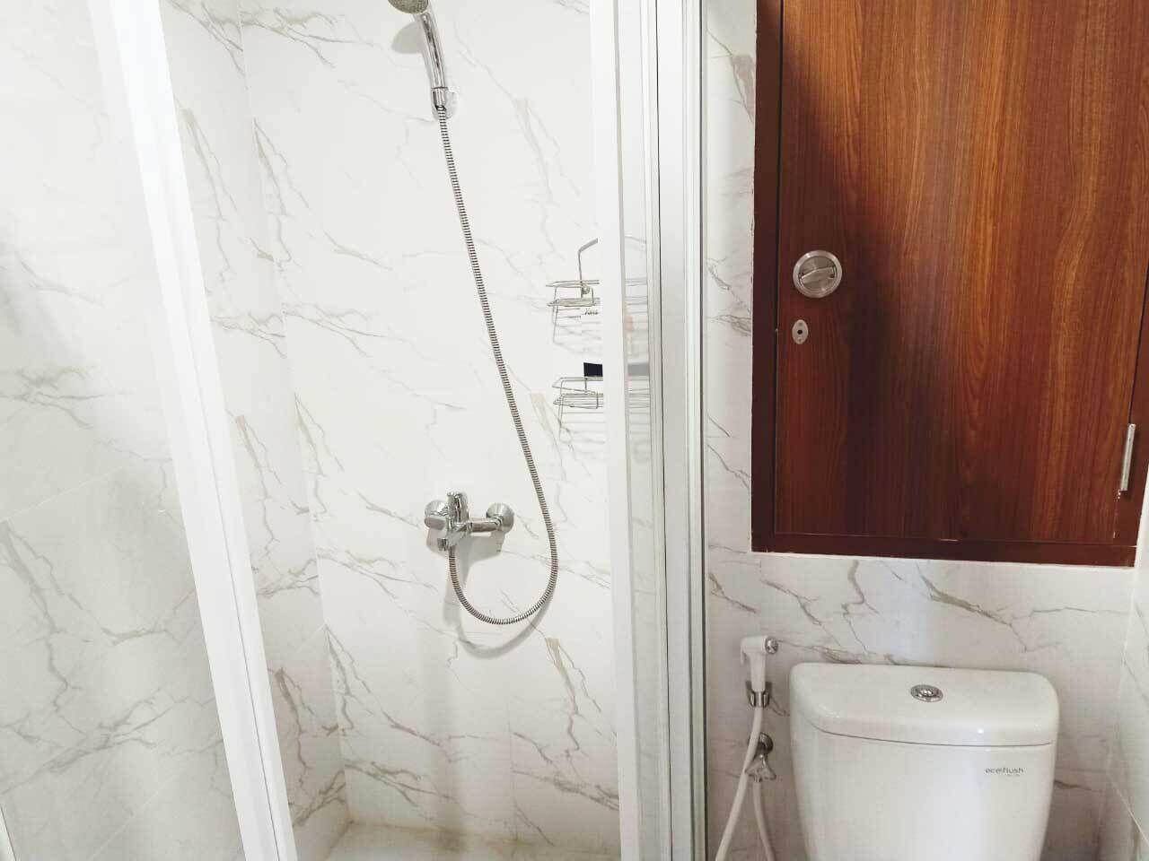 Un baño con pared de mármol, ducha con cabezal de ducha manual, inodoro y armario de madera.