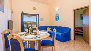 Un comedor con una mesa preparada para dos personas, un sofá azul y vista al mar.