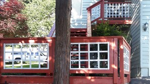 Ein Haus mit rotem und weißem Zaun, einem großen Baum und einem Blumentopf.