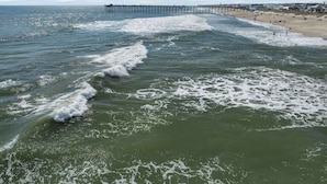 A beach with waves, a pier, and a distant shoreline.
