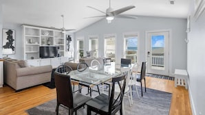 A modern living room with a glass dining table, a sofa, a TV, and a ceiling fan.