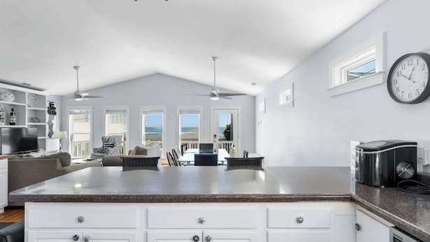 A modern kitchen with white cabinetry, a granite countertop, and a built-in island. There is a dining area with a table and chairs, and a large clock on the wall.