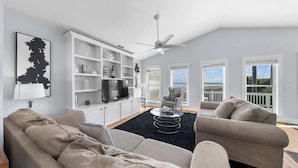 A modern living room with a sofa set, a TV, shelves with decorative items, and a view of the outdoors.