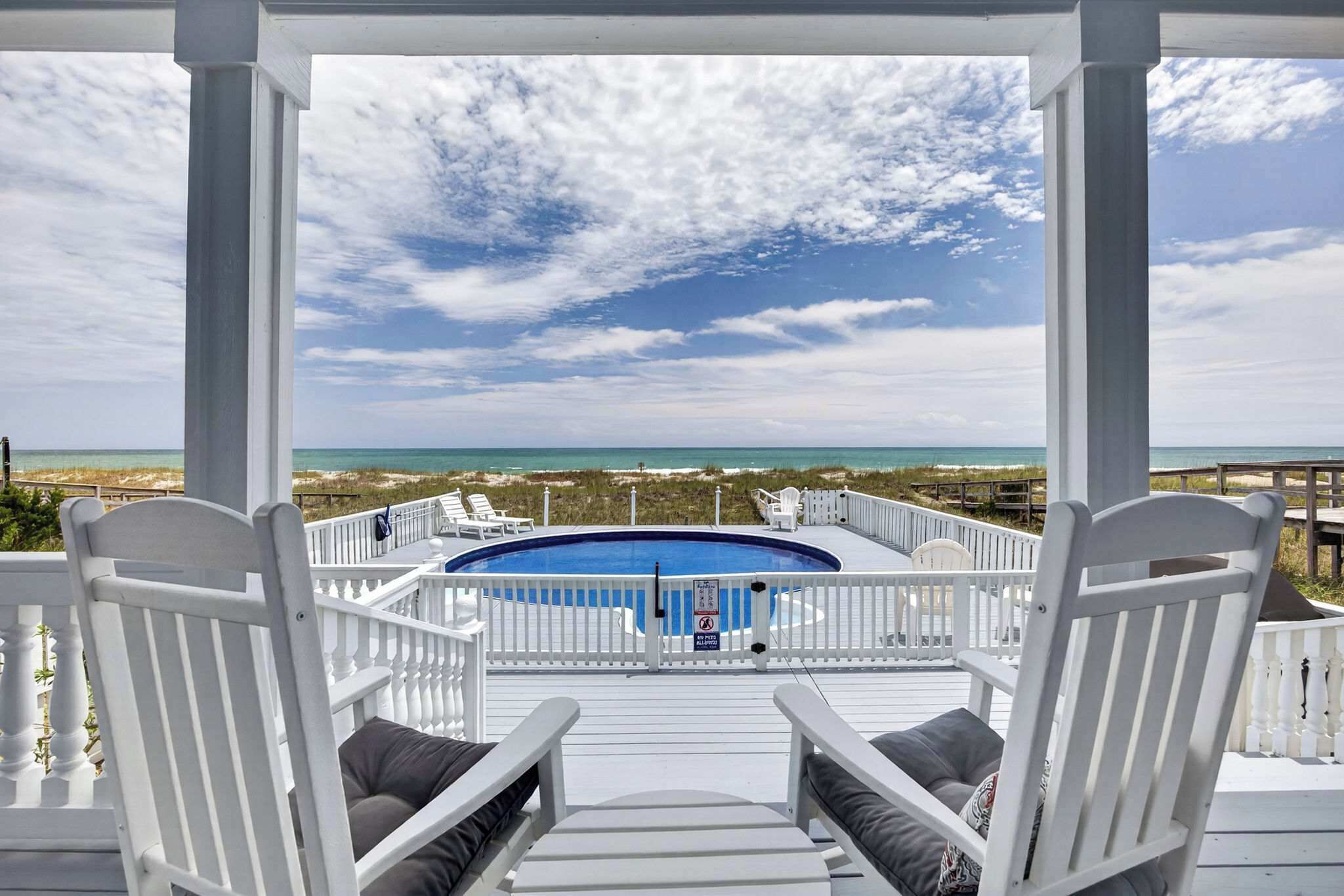 A pool deck with a view of the ocean, white chairs, and a clear sky.
