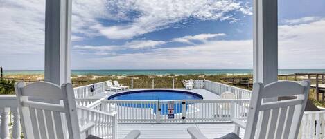 A pool deck with a view of the ocean, white chairs, and a clear sky.