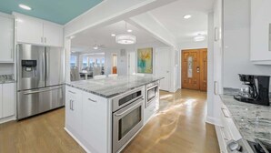 A modern kitchen with white cabinetry, stainless steel appliances, and a marble countertop. - Sea2Sky by Carolina Getaway - Oceanfront Home w/ Private Pool & Heated Spa (Kure Beach)