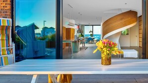 Un intérieur moderne avec une grande fenêtre, un escalier en colimaçon et un coin repas offrant une vue sur la mer.