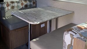 Une cuisine compacte pour camping-car, dotée d’une table intégrée, d’un four à micro-ondes et d’une fenêtre avec stores.