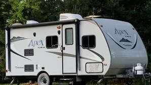 Un camping-car blanc arborant les marques « Apex » et « Coachmen », doté d’un aménagement compact comprenant un petit coin cuisine et un espace de couchage.