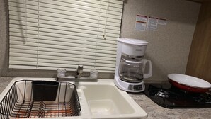 Une cuisine équipée d’un évier, d’une machine à café et d’une casserole rouge posée sur le plan de travail.