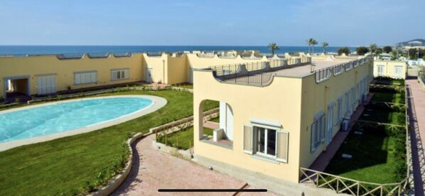 A resort with a swimming pool, a well-maintained lawn, and a view of the sea. - P I A Beach House (Bacoli)