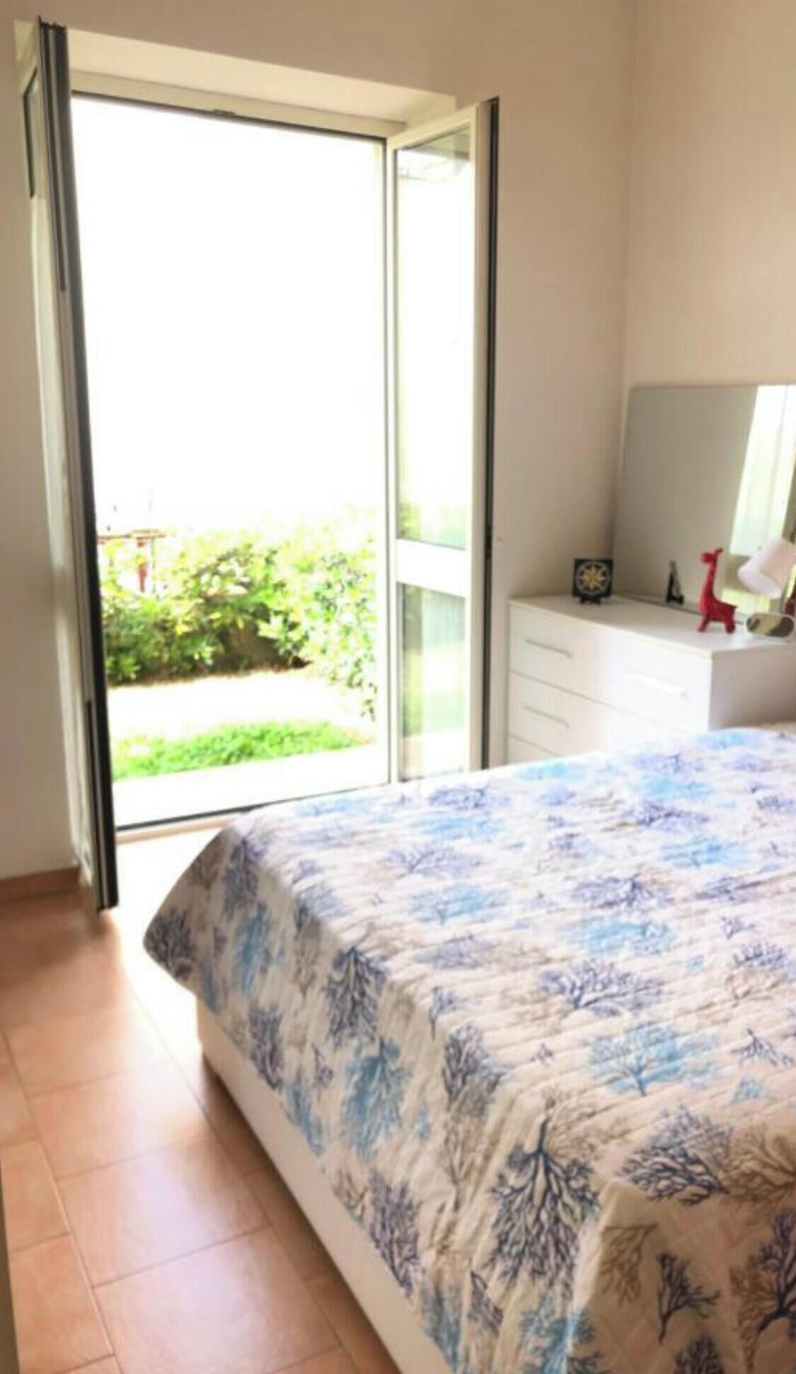 A bedroom with a bed, a dresser, a mirror, and a sliding glass door leading to a balcony.