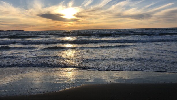 Une plage avec des vagues et un coucher de soleil.