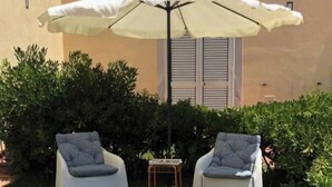 Un espace extérieur aménagé avec deux chaises blanches, une table en verre et un parasol blanc.