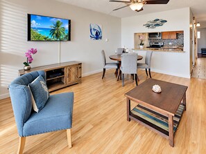 A living room with a TV, a dining area with chairs, a coffee table, and a kitchen in the background.