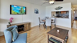 A living room with a sofa, coffee table, and a TV mounted on the wall. - Where Turquoise Waters Beckon Kihei Condo Ocean Views Rooftop Garden Pool (Kihei)