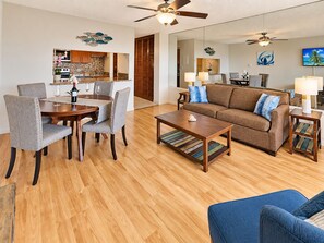 A living room with a sofa, coffee table, and dining area with chairs. - Where Turquoise Waters Beckon Kihei Condo Ocean Views Rooftop Garden Pool (Kihei)