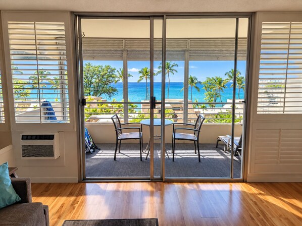 A room with a sliding glass door leading to a balcony with a view of the ocean and palm trees.