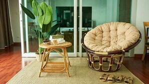 A room with a large window, a wicker chair, a small table with a plant, and a pair of slippers on the floor. - Bellevue Boutique Bangkok (Bangkok)
