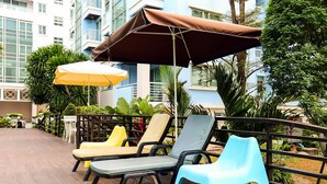 Outdoor lounge chairs and umbrellas on a wooden deck with a view of a building and greenery. - Bellevue Boutique Bangkok (Bangkok)