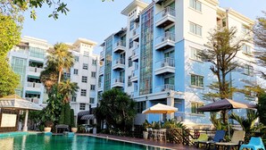 A swimming pool with lounge chairs and umbrellas, surrounded by multi-story buildings with balconies. - Bellevue Boutique Bangkok (Bangkok)