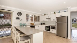 Una cocina moderna con muebles blancos, un refrigerador de acero inoxidable y un comedor con una barra alargada y sillas.
