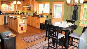 A kitchen with wooden cabinets, a central island, and a dining area with a table and chairs. - Woodland Trails Cabin on 130 acres with wildlife and miles of private trails (Hinckley)