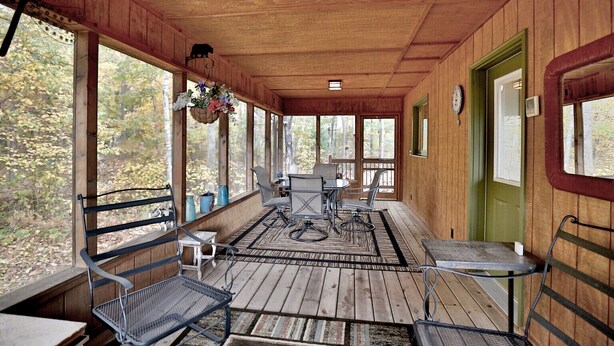 A covered porch with wooden flooring, metal chairs, a table, and a hanging flower basket. - Woodland Trails Cabin on 130 acres with wildlife and miles of private trails (Hinckley)