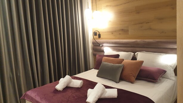 A hotel room with a wooden headboard, a bed with multiple pillows, and a large window with curtains.