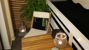 A wooden bench with a cushion, a Buddha statue, a potted plant, and decorative items on a balcony railing.