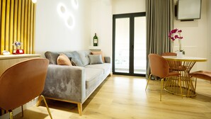 A modern living room with a sofa, chairs, a dining table, and a TV mounted on the wall.