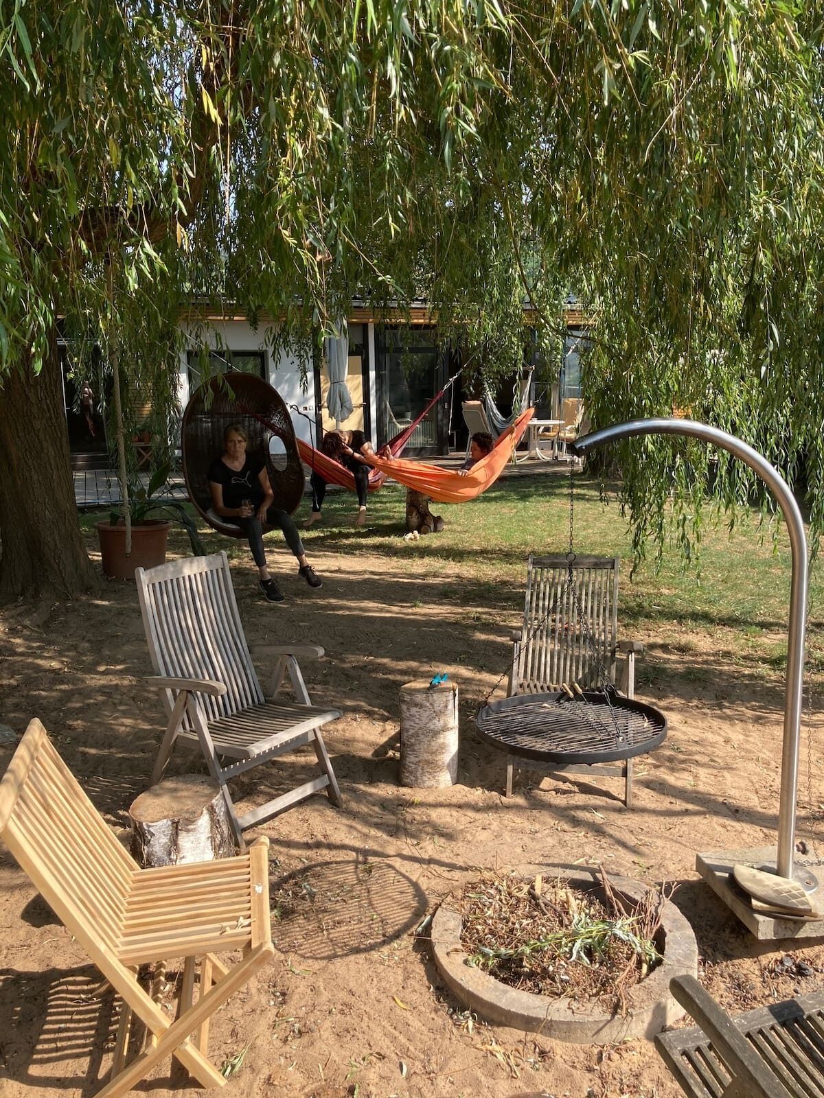 An outdoor seating area with wooden chairs and a hammock under a tree.