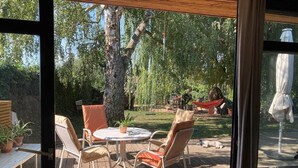 An outdoor patio with a round table and chairs, surrounded by a wooden deck and a grassy area with trees. - Ferienidylle Haus Königsberg, Child-friendly, Dog-friendly, Barrier-free (Michelstadt)
