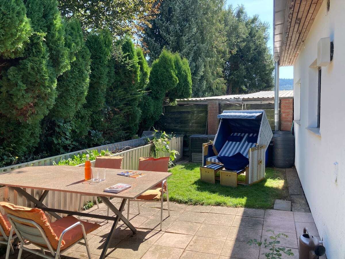 Een terras met een tafel en stoelen, een barbecue en een kleine tuin met bomen en een hek.